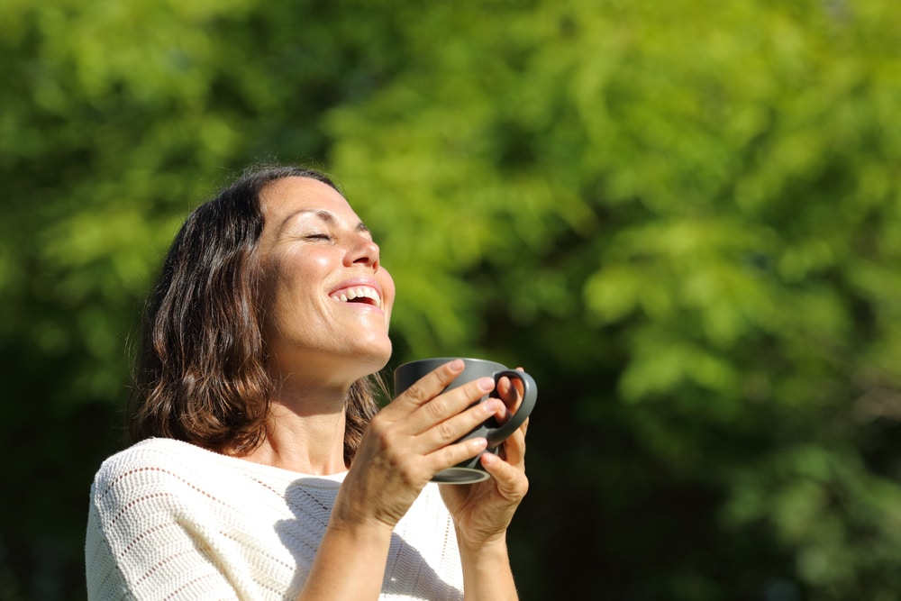 Woman smiling and taking a deep breath outdoors surrounded by greenery