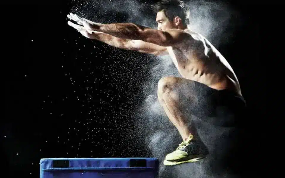 Athlete performing an explosive box jump in a dark studio