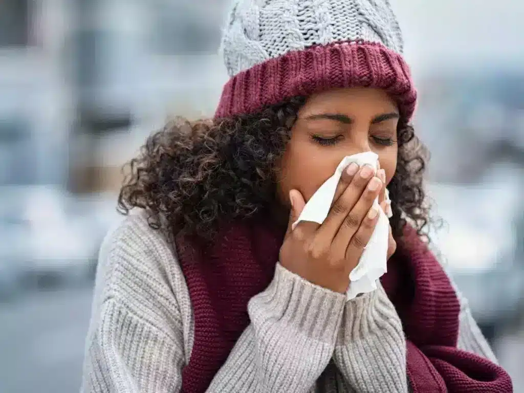 Woman outdoors in winter clothing blowing her nose with a tissue