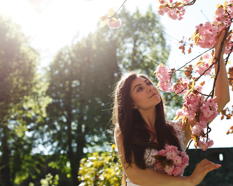 Woman smiling outdoors near a flowering tree with sunlight