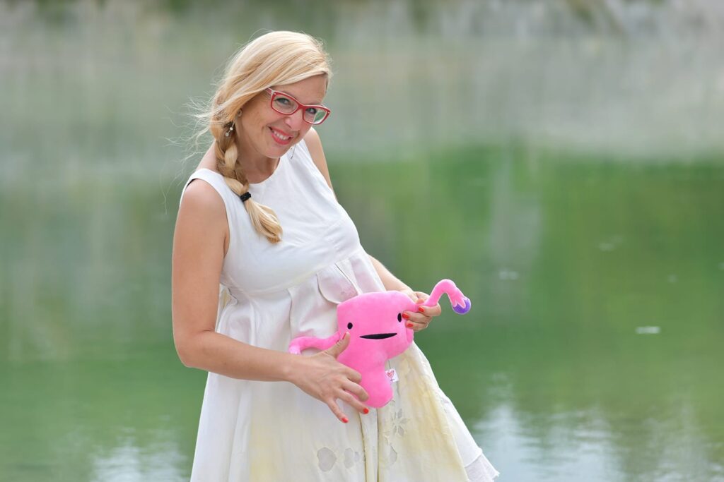 Pregnant woman outdoors holding a pink item near a lake