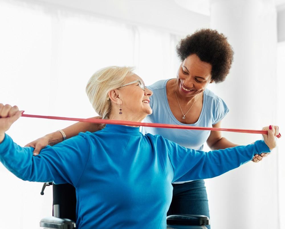 Woman helping an older man in a wheelchair with a resistance band exercise