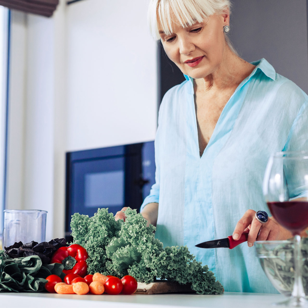 Woman chopping vegetables in a kitchen while holding a glass of wine